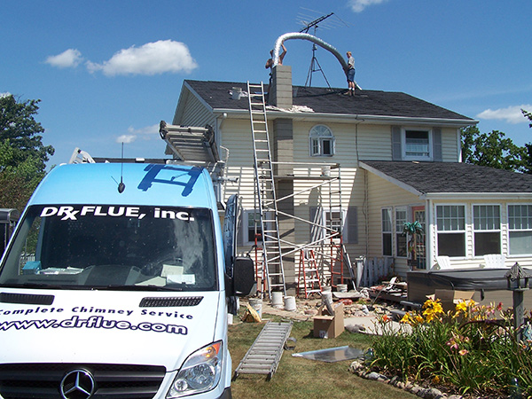 Doctor Flue installing a new chimney liner on the roof of a home with the Doctor Flue sprinter van in the foreground.