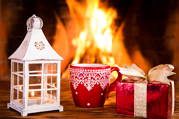 A candle, mug and wrapped gift are set in front of a fire in a fireplace