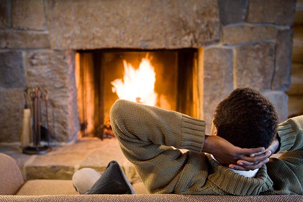Man on couch relaxes in front of roaring fire in fireplace.