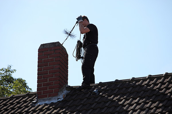 Chimney sweep on a roof using a wire brush to clean a chimney flue