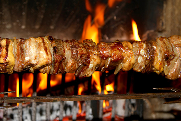 Skewers of meat being cooked in an indoor fireplace.