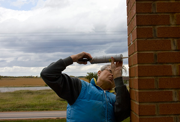 Woman repairing a brick chimney with caulk.