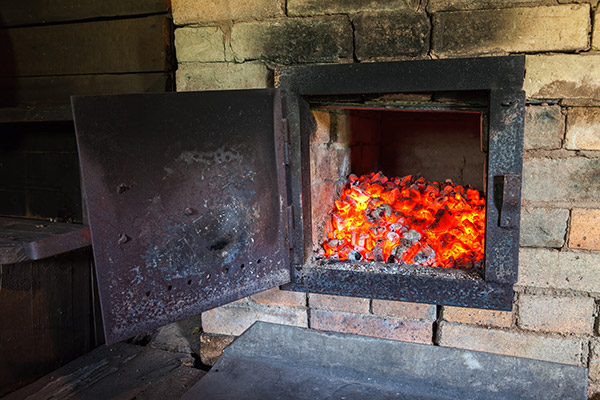 Old corroded wood-burning stove with a glowing fire inside. 