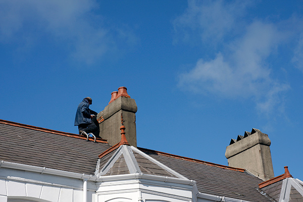 Workman repairing a chimney stack on top of a roof.
