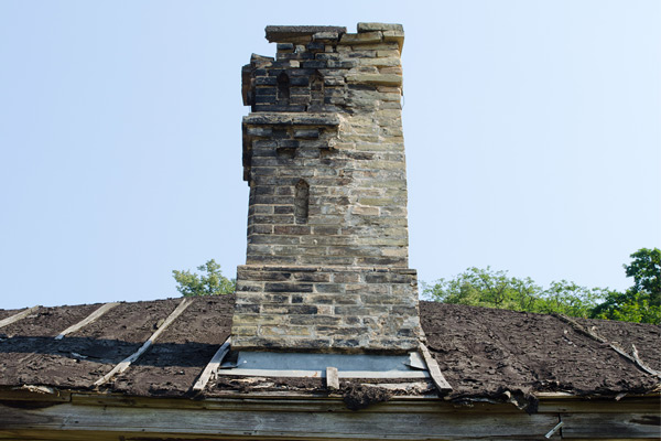 A damaged chimney with missing bricks and scorch marks on a damaged roof due to chimney fire.