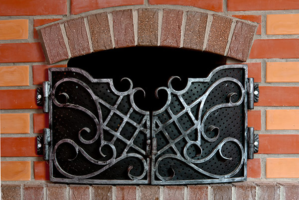 Brick fireplace with a closed iron gate covering the opening.