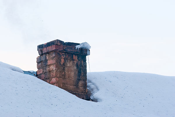 Scorched brick chimney on snow covered rooftop.