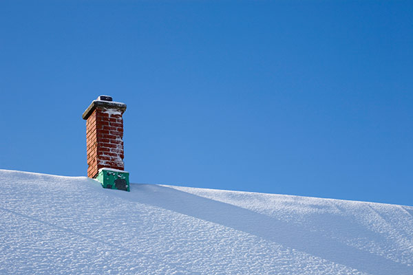 A chimney on a snowy roof at risk for fireplace drafts.