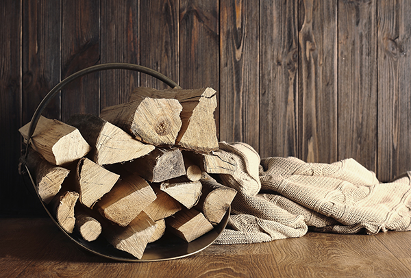 Firewood stacked in a metal, hearthside, log-holder basket.