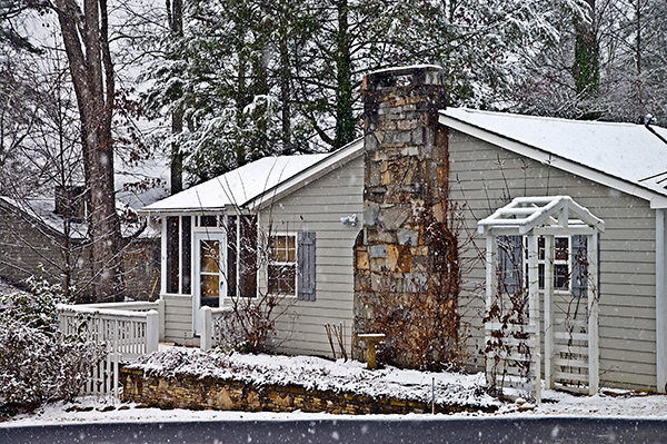 Snowfall on a house with a large stone chimney means it’s time for winter chimney prep.