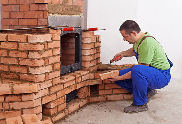 A man lays bricks to build an outdoor fireplace. Fireplace safety codes need to be followed when installing a fireplace. 