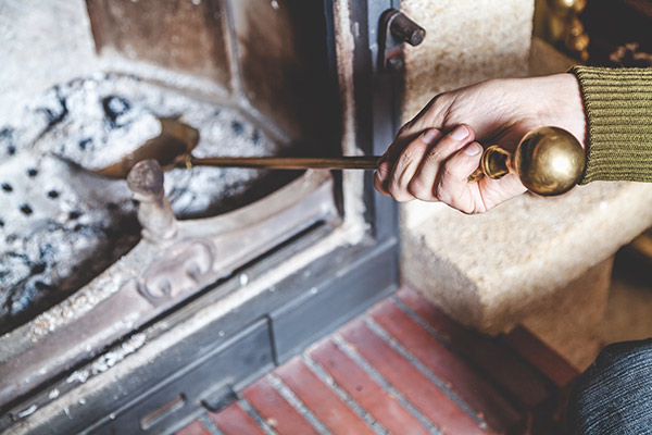 A homeowner who knows how to clean a fireplace removing ash