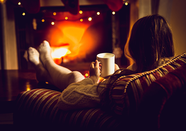 Woman sitting comfortably at her fireplace with tea