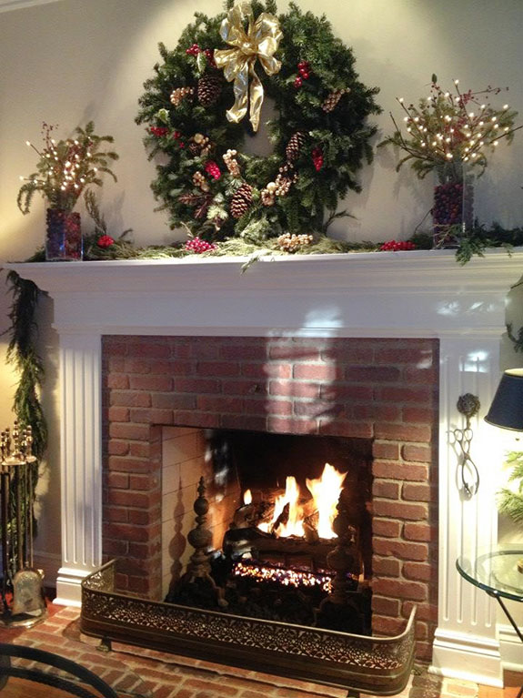 mantel decorated in classic christmas style with wreath, pine cones, pillar candles, and ribbon