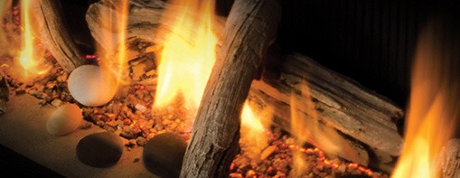Close-up of gas fireplace flames among ceramic logs, stones and glowing embers